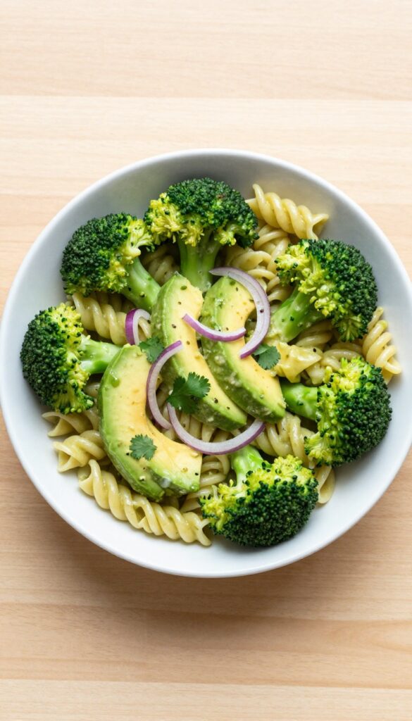 Creamy avocado and broccoli pasta salad in a white bowl on a wooden table.