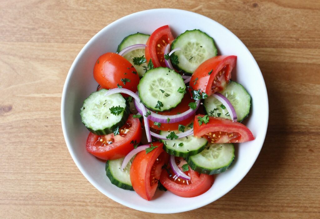 Colorful cucumber tomato salad with red onion and fresh herbs in a white bowl