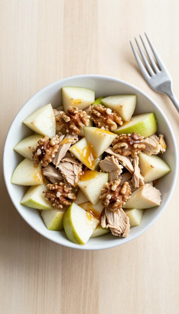 Chicken salad with apple and walnuts in a white bowl, overhead view