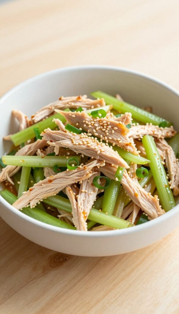 Ginger sesame chicken salad with celery and scallions in a white bowl on a wooden table