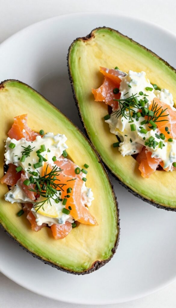 Creamy avocado boats filled with smoked salmon and cream cheese, garnished with dill and chives on a white plate.